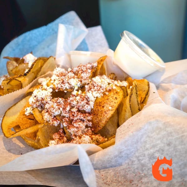 Crispy potato chips topped with crumbled feta cheese and red spices, served with a side of white sauce.