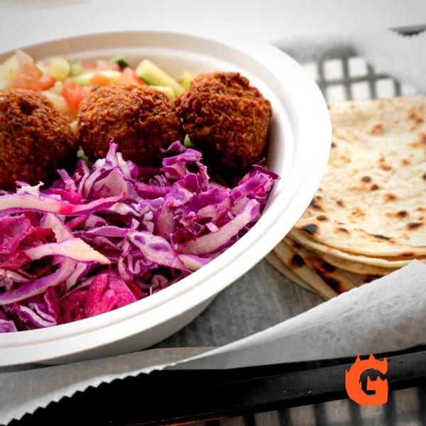 Gita Pita falafel bowl with red cabbage, salad, and a stack of pita bread.