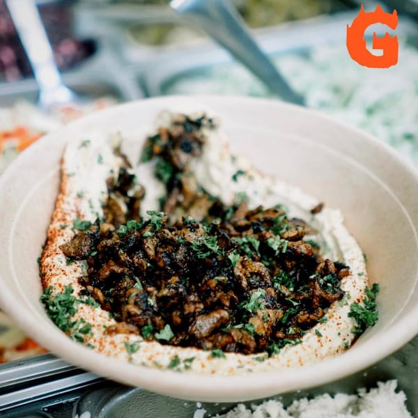 A bowl of Gita Pita hummus topped with seasoned meat, paprika, and fresh parsley.