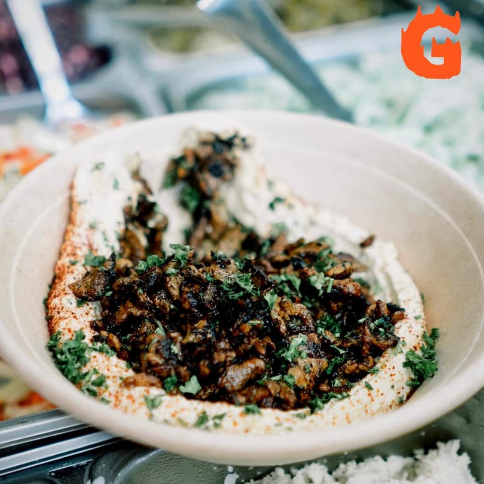A bowl of Gita Pita hummus topped with seasoned meat, paprika, and fresh parsley.