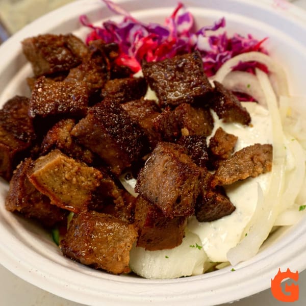 A Gita Pita bowl with seasoned meat, white sauce, sliced onions, and red cabbage.